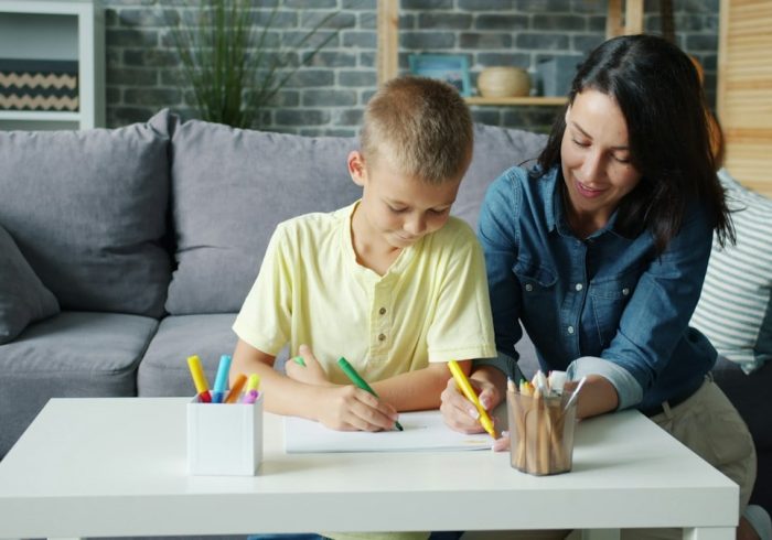 Small boy is drawing with markers together with caring mother in cozy room at home enjoying activity making picture. Creative kids and loving parents concept.