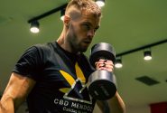 Muscular man exercising with a dumbbell in a modern gym setting, emphasizing strength and fitness.